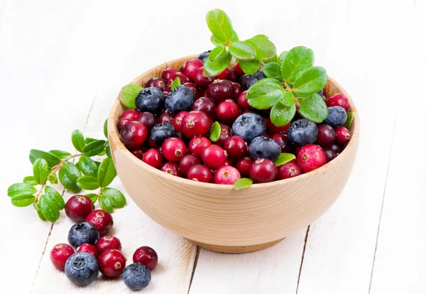 Blueberry and cowberry with green leaflets in wooden cup — Stock Photo, Image