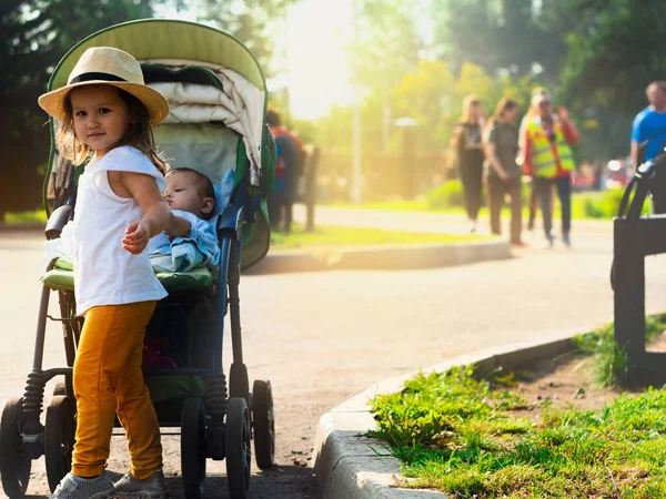 Güneşli yaz fotoğrafında şapkalı bir çocuk bebekle fayton yuvarlıyor.