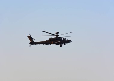Mavi gökyüzünde bir askeri helikopter uçuyor.