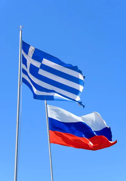 Flags of Greece and Russia are flying in the wind against the blue sky