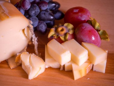 Traditional Greek smoked cheese Metsovone on a wooden board with grapes and persimmons from the village Metsovo in Greece