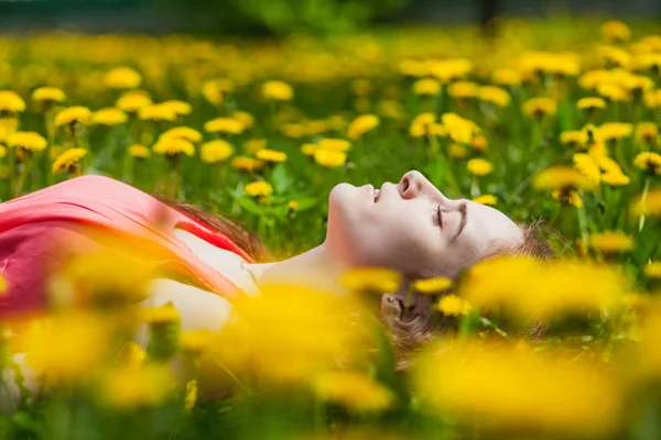 Mooi meisje liggend op het gebied van paardebloemen — Stockfoto