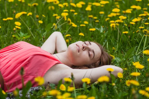 Mooi meisje liggend op het gebied van paardebloemen — Stockfoto