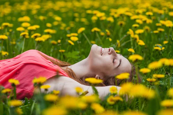 Schönes Mädchen liegt auf dem Feld von Löwenzahn — Stockfoto