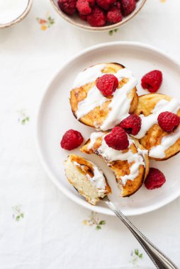 Beyaz tabakta süzme peynirli krep. Ahududu ve ekşi kremalı Syrniki. Lezzetli ev yapımı kahvaltı ya da öğle yemeği