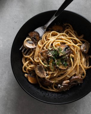 Tabakta mantarlı, yeşil peynirli ve arka planda baharatlı makarna. Siyah kasede servis edilen mantarlı makarna. Sağlıklı vejetaryen yemekleri ve yemekleri