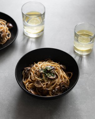 Tabakta mantarlı, yeşil peynirli ve arka planda baharatlı makarna. Siyah kasede servis edilen mantarlı makarna. Sağlıklı vejetaryen yemekleri ve yemekleri