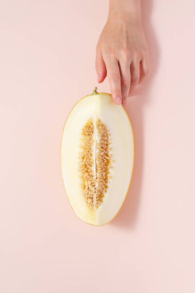 A hand holds a melon on a light pink background, copy space