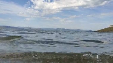 Clear water. Small waves. Mountains in the distance. Clouds. The splash of water.