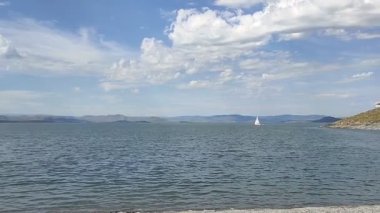 Clear water. Small waves. Mountains in the distance. Clouds. Stones at the bottom of the water. Lake. The yacht is moving.