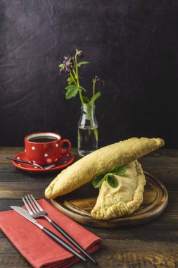 Çikolatalı sandviç büyüklüğünde calzone ve koyu ahşap masada servis edilen kahve ile kahvaltı..