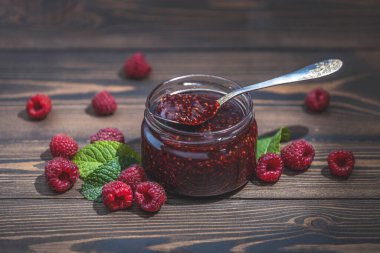 Ev yapımı ahududu reçeli ya da cam kavanozda marmelat ve ahşap masada olgun ahududu.