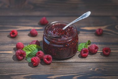 Ev yapımı ahududu reçeli ya da cam kavanozda marmelat ve ahşap masada olgun ahududu.