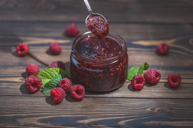 Ev yapımı ahududu reçeli ya da cam kavanozda marmelat ve ahşap masada olgun ahududu.