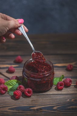 Ev yapımı ahududu reçeli ya da cam kavanozda marmelat ve ahşap masada olgun ahududu.