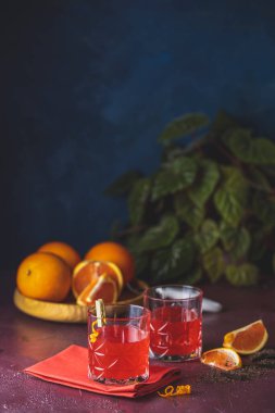 İki bardak çikolatalı kırmızı turuncu negroni, bir italyan kokteyli, bir aperatif, ilk kez 1919 'da Firenze, İtalya' da karıştırılmış, koyu kırmızı bordo masasındaki malzemelerin sunduğu alkollü acı kokteyl..