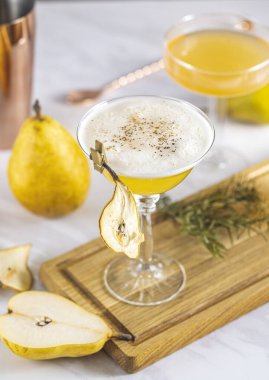 Armut Elder Kokteyli. Şampanya kadehi armut püresi kokteyli ya da içindekiler ve açık gri masa yüzeyindeki bar aletleriyle çevrili moktakolar ile dolu.