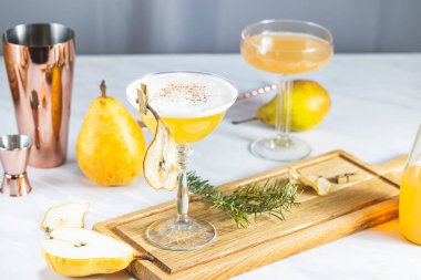 Armut Elder Kokteyli. Şampanya kadehi armut püresi kokteyli ya da içindekiler ve açık gri masa yüzeyindeki bar aletleriyle çevrili moktakolar ile dolu.