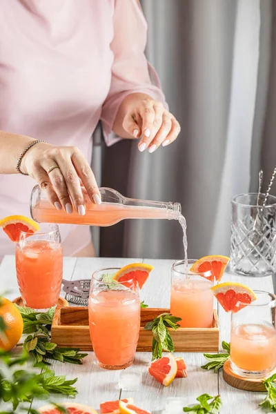 Grapefruit kokteyli hazırlayan gerçek bir kadın. İçindekiler ve açık gri masa yüzeyindeki bar aletleriyle çevrili kokteyller. İçmeye hazırım.