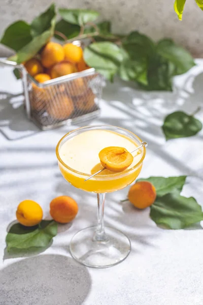 Elegant glass of Apricot Lady Cocktail or mocktails surrounded by ingredients and fresh fruits on gray table surface, ready for drinking