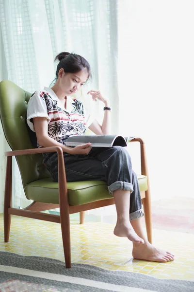 Asian girl reading while sitting in an easy chair — Stock Photo, Image