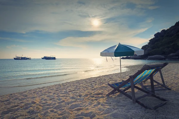 Cadeiras de madeira cama e guarda-chuva na praia de areia ao pôr do sol — Fotografia de Stock