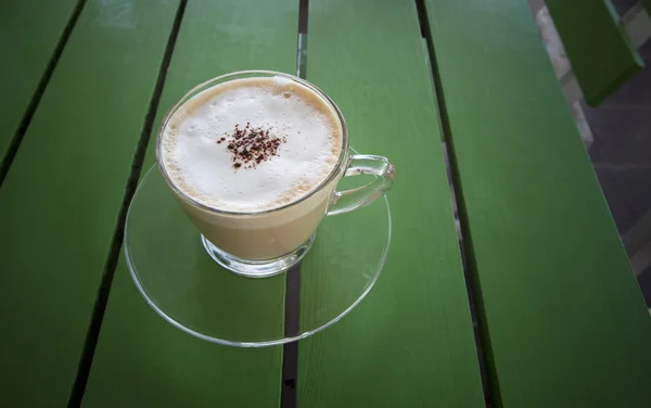 Heißer Cappuccino-Kaffee im Glasbecher auf grünem Tisch — Stockfoto