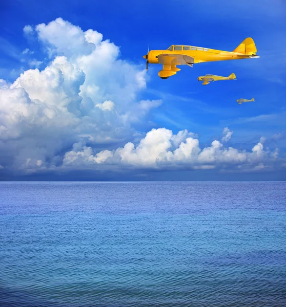 Três de avião amarelo voando sobre a água do mar — Fotografia de Stock