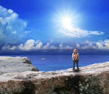 Back of young man standing on rock cliff and looking to sea clipart