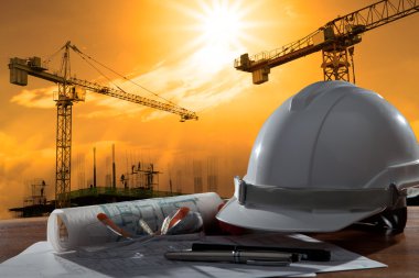 Safety helmet and architect pland on wood table with sunset scen clipart