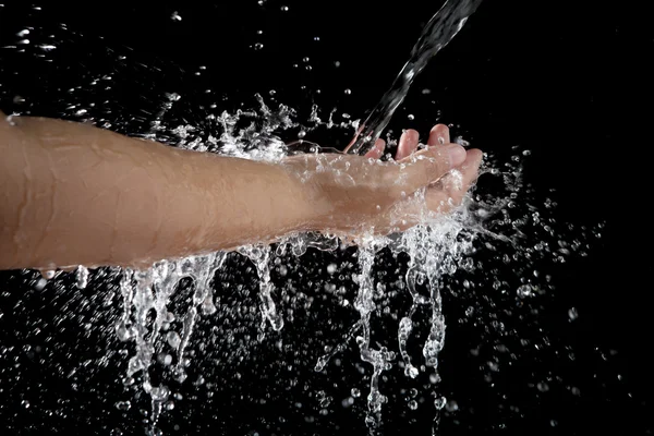 Mão e derramamento de água espirrando sobre fundo preto — Fotografia de Stock