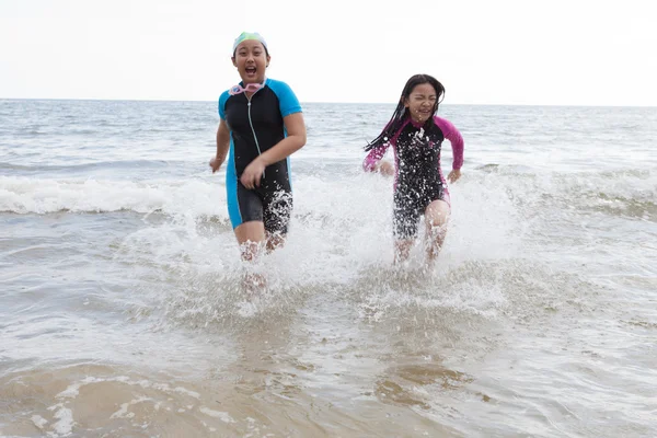 Две девушки в мокрых костюмах играют на пляже со счастливыми эмоциями — стоковое фото