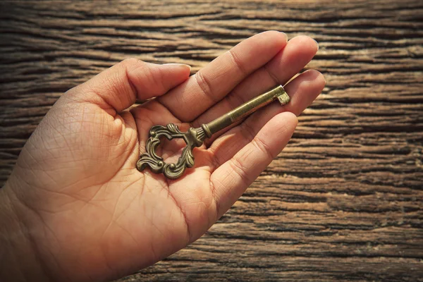 Abstract of metal key on left hand against textured of bark wood — Stock Photo, Image