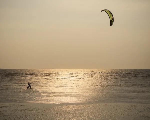 Homem com kite surving em pé na água do mar contra o sol da noite — Fotografia de Stock