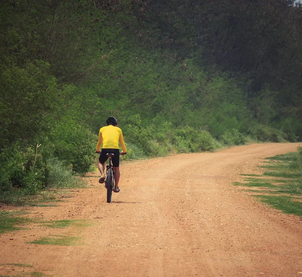 Jovem montando bicicleta de montanha em uso de estrada empoeirada para esporte leisu — Fotografia de Stock