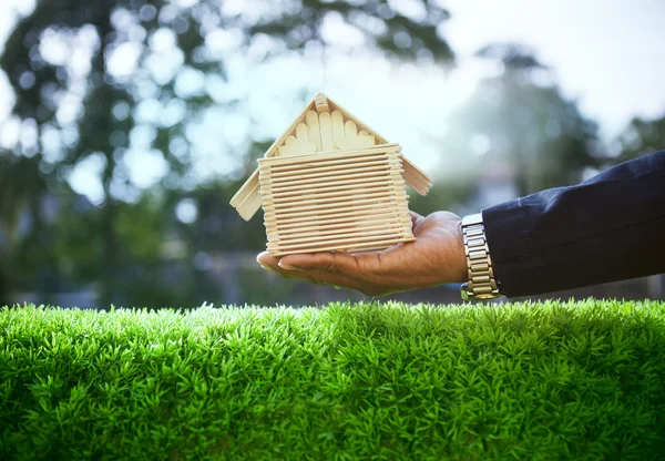 Mano di uomo d'affari e modello di casa in legno su bella gra verde — Foto Stock