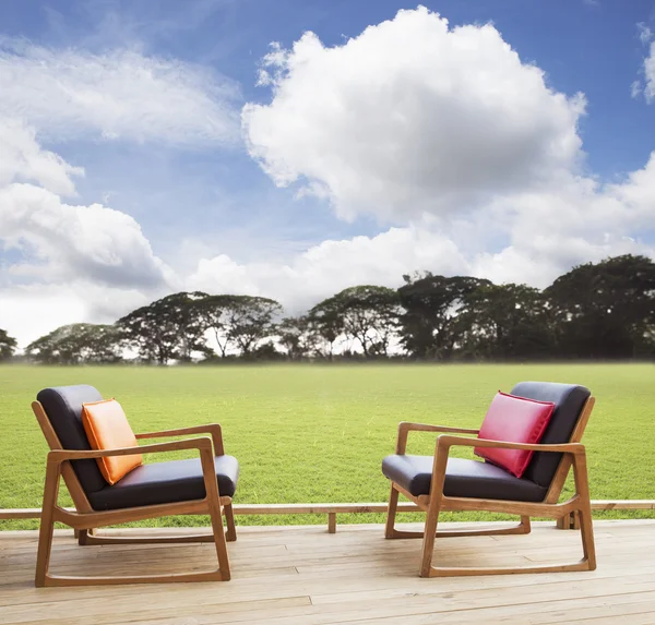 Расслабьтесь стулья на деревянной террасе с травяным полем и красивым небом — стоковое фото