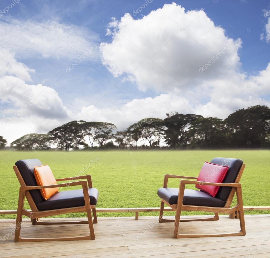 Relax chairs on wood terrace with grass field and beautiful sky