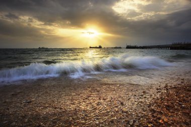 çakıl plaj güneş karşı sıçramasına dalga deniz gökyüzü ve comme ayarla