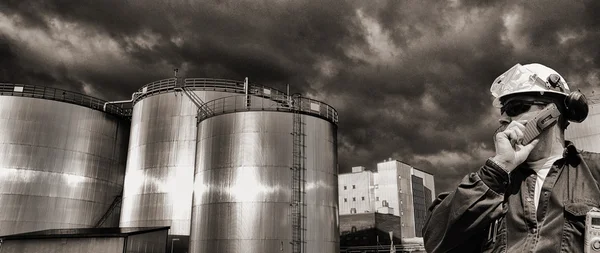 Trabajador petrolero y torres de almacenamiento de combustible al atardecer — Foto de Stock