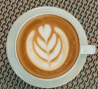 Yakın plan. Cam sehpanın üzerinde Latte sanat kahve fincanı. Bulanık yaprak yansıma arkaplanı.