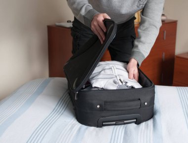 man prepares suitcase leaning on the bed