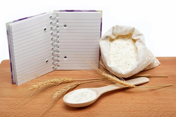 Recipe Book and flour in a sack with a spoon on a wooden table. — Stock Photo, Image