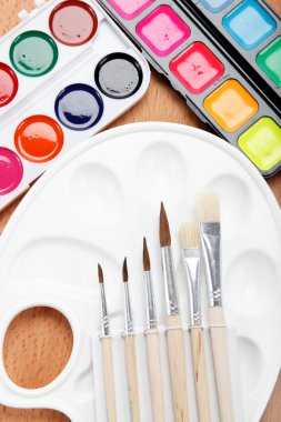 pintura, paleta y pinceles en una mesa de madera.