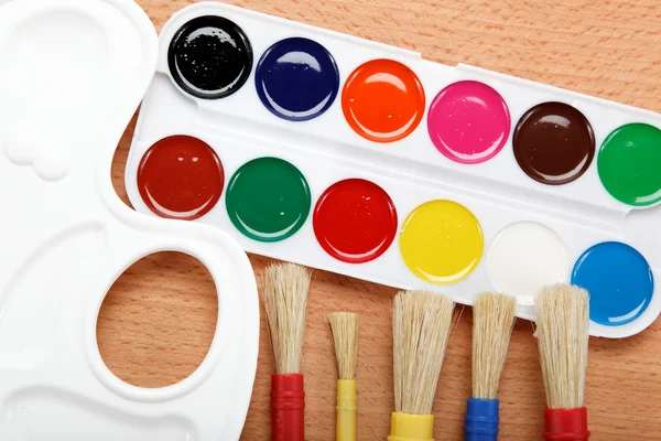 Pintura, paleta e pincéis em uma mesa de madeira . — Fotografia de Stock