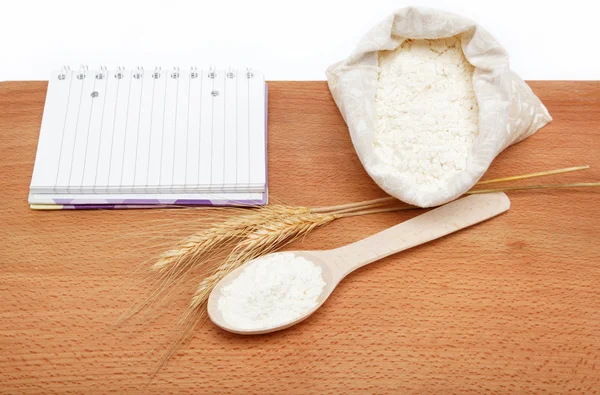 レシピ本や木製のテーブル スプーンで袋に小麦粉. — ストック写真
