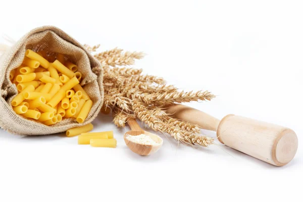 Pasta in a canvas bag, flour in a wooden spoon and ear on white — Stock Photo, Image