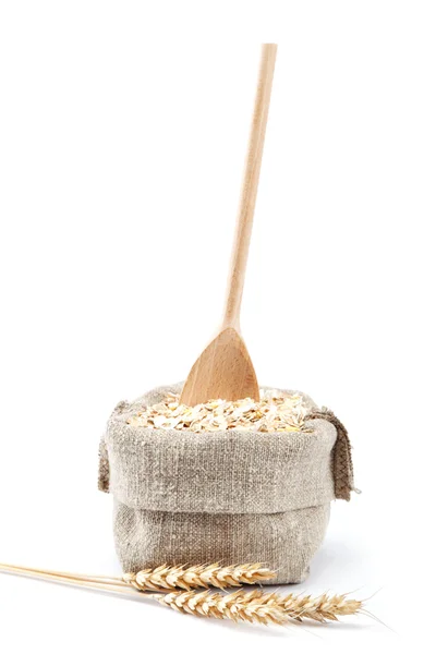 Avena enrollada en una bolsa con una cuchara de madera y espigas de trigo aisladas —  Fotos de Stock