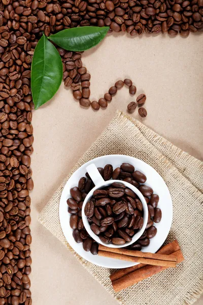 Cup with coffee beans and cinnamon sticks on sackcloth. — Stock Photo, Image