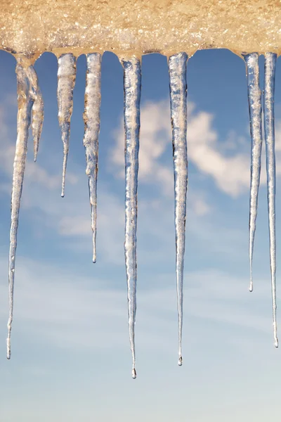 Icicles in the sunny day against a blue sky with white clouds. — Stock Photo, Image